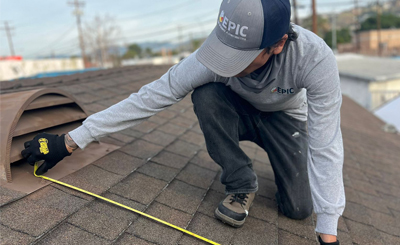 A worker from Epic Roof Replacement measures a roof vent with a tape measure, showcasing attention to detail and craftsmanship.